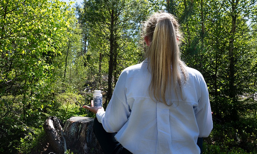 Kvinna sitter ner i skogen med en burk Healthwell Magtein Magnesium L-threonate i sin hand.